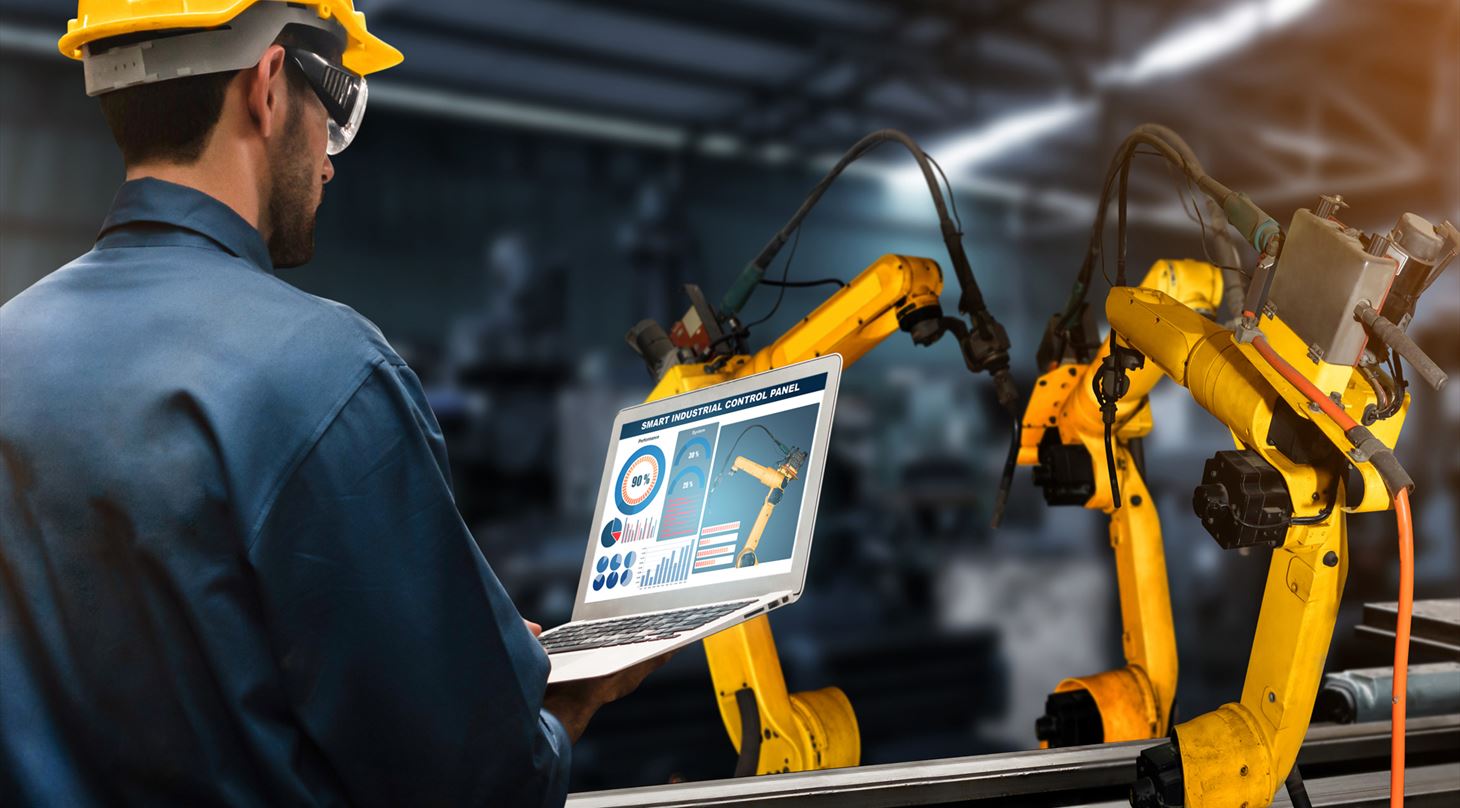 Billede af mand med en computer, der styrer nogle robotter, der arbejder på en produktion